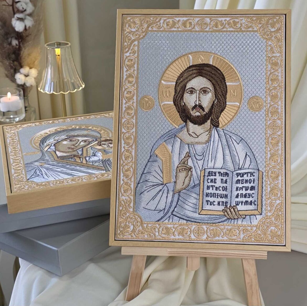 Вишита ікона Спасителя на мольберті, позаду Казанська ікона на сірих подарункових коробках і свічка