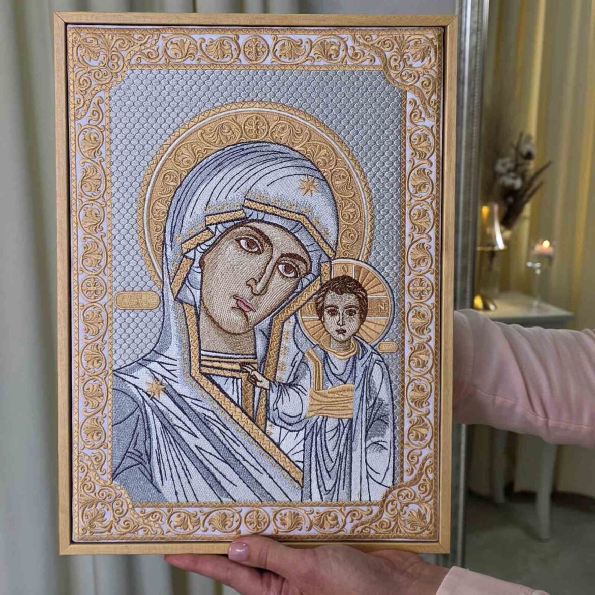 Вишита ікона Спасителя на мольберті, позаду Казанська ікона на сірих подарункових коробках і свічка