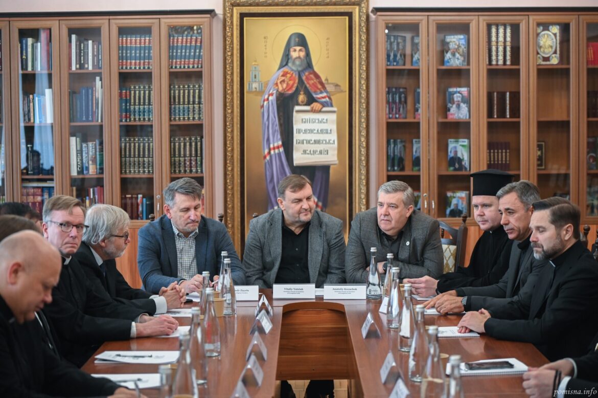 Учасники зустрічі за столом на тлі великого образу святителя Петра Могили з сувоєм «Київська православна богословська академія»