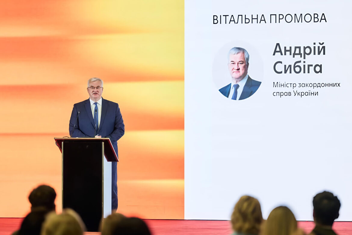 Андрій Сибіга за трибуною, на екрані напис «Вітальна промова. Андрій Сибіга, Міністр закордонних справ України»